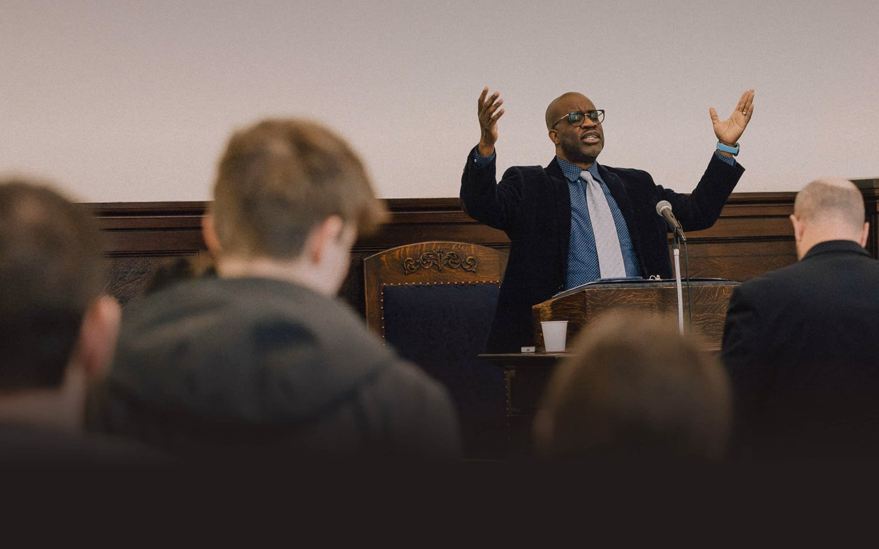 Pastor preaching from the pulpit with hands raised as the congregation looks on